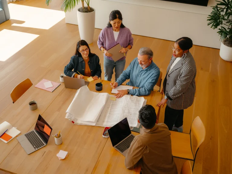 Equipe de PMO vista de cima planejando portfólio com plantas de projeto na mesa