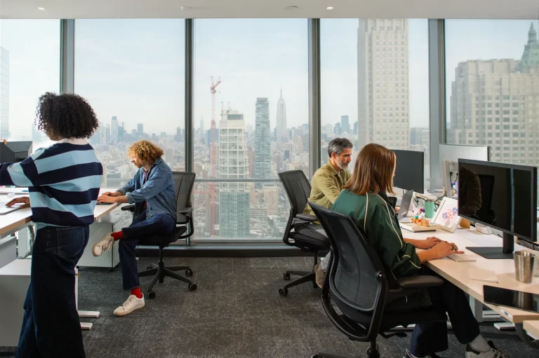 Escritório de tecnologia com vista para a cidade, times operando dados de receita em múltiplos monitores